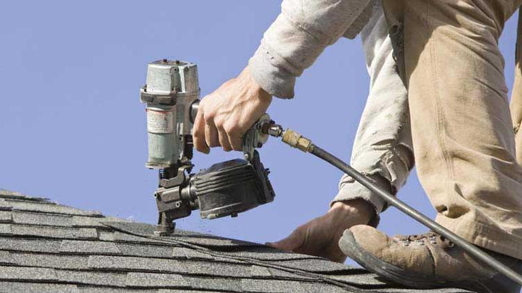 Man on 屋顶 fixing shingles with a nail gun.